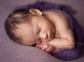 Photo nouveau-ne Bébé endormi en boule dans un textile violet